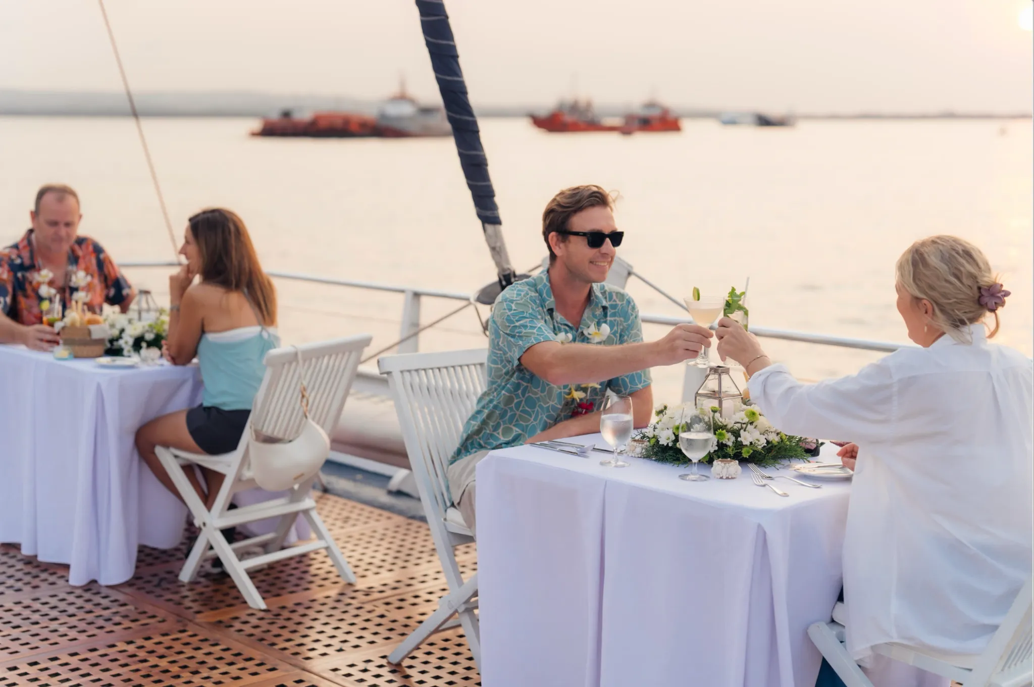 Couple enjoying a romantic evening dinner cruise in Bali, toasting cocktails on a luxury Aristocat catamaran with ocean views.